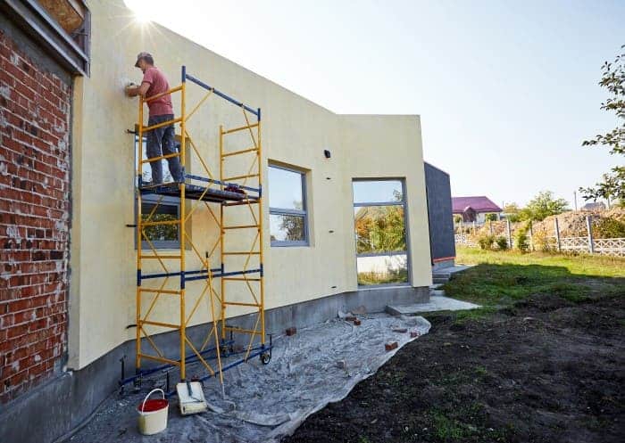 Person beim Arbeiten an einer Hausfassade auf einem zuvor aufgebautem Arbeitsgerüst